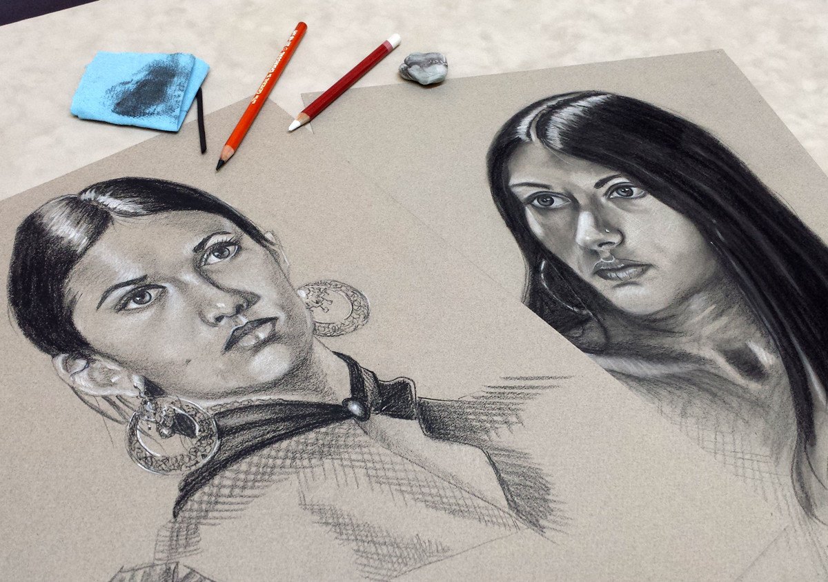 Two charcoal portrait drawings with pencils and an eraser on the drawing table